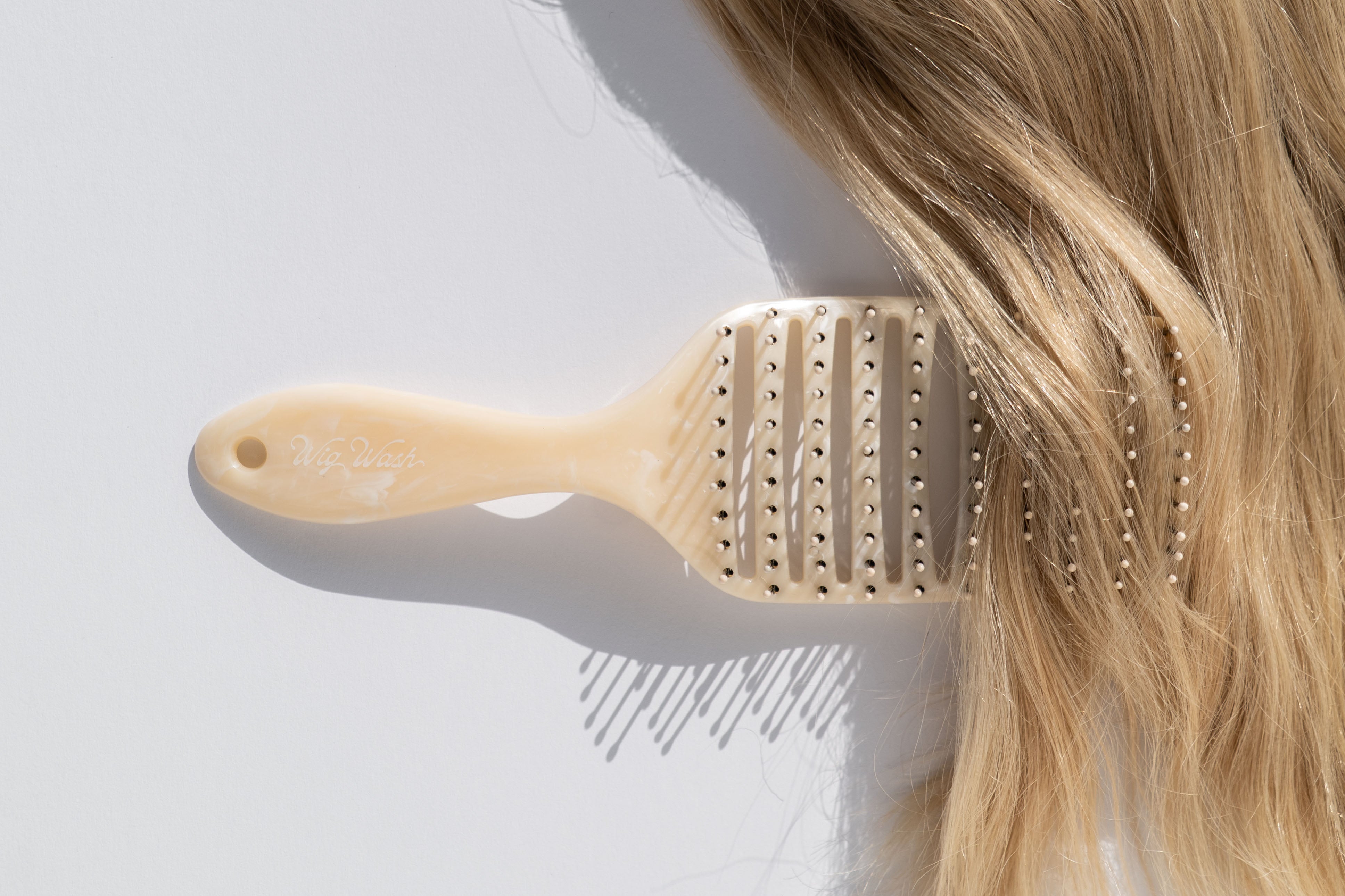 Vent hair brush being used on blonde human hair wig against a light background