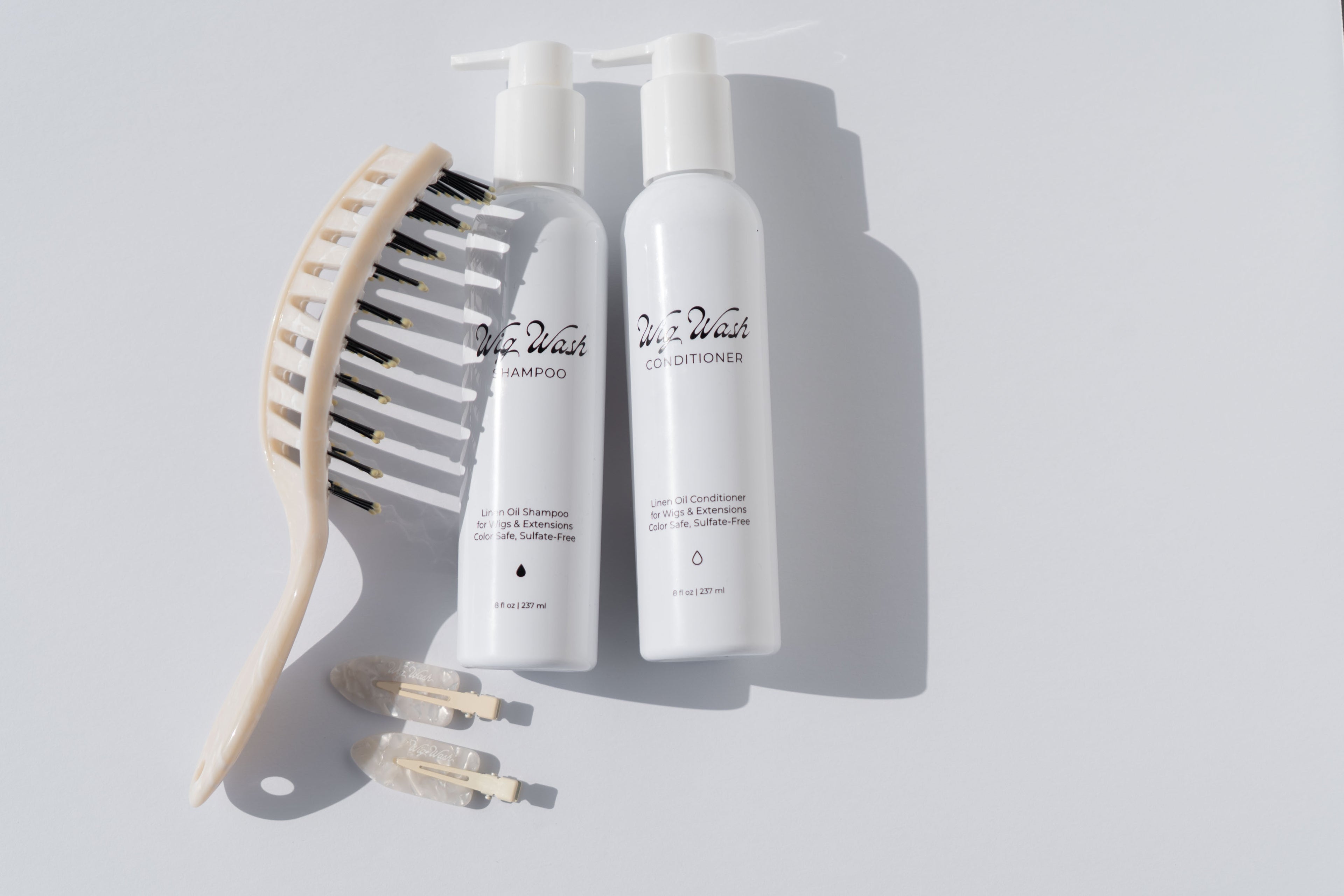 Two bottles of 'WIG WASH shampoo and conditioner with a brush on a light gray background